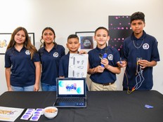 Students smile while standing behind a table with a laptop and the Utensil Gadget prototype.